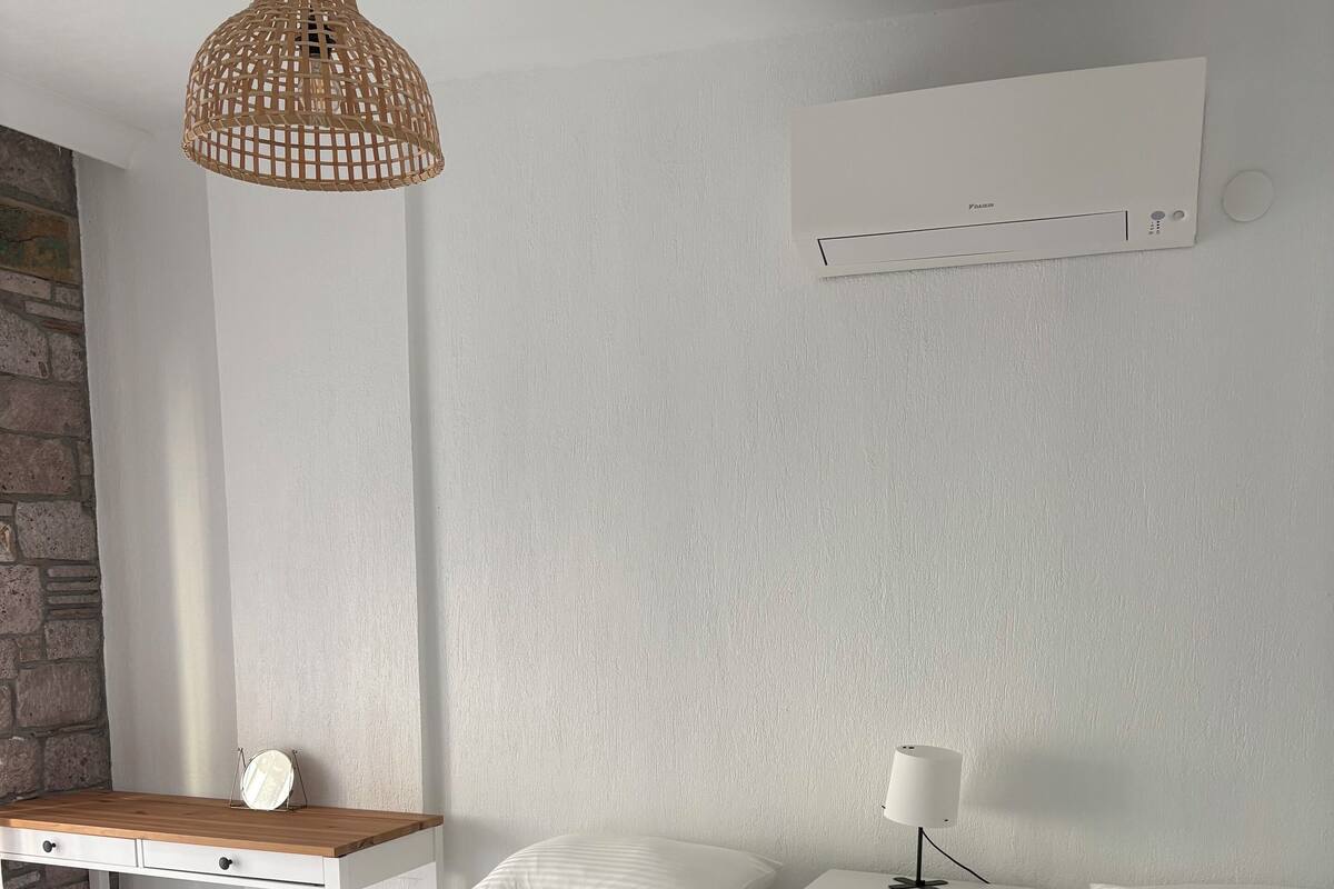 Une chambre avec deux lits, un bureau, une chaise, un luminaire suspendu et un climatiseur fixé au mur.
