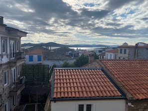 A coastal town with terracotta-tiled rooftops, stone buildings, and a view of the sea and mountains in the distance. - MyWayHoliday (Ayvalik)