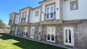 A multi-story building with stone and stucco exterior, multiple balconies, and large arched windows. - MyWayHoliday (Ayvalik)