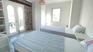 A bedroom with two beds, a stone wall, a window, and a door with glass panels. - MyWayHoliday (Ayvalik)