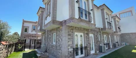 Una casa de dos pisos con fachada de piedra, ventanas amplias y un balcón.