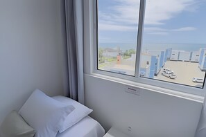 A hotel room with a bed, a window with a view of a parking area and buildings. - Solarium Beach Club - Apartamento T1.505 (Itapoá)