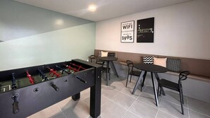 A modern room with a foosball table, a sofa, and two small tables. - Solarium Beach Club - Apartamento T1.505 (Itapoá)