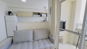 Una stanza compatta con divano, angolo cottura e un balcone con porta in vetro.