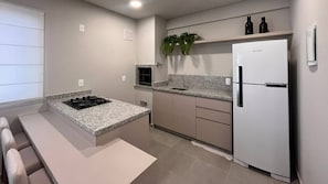 A modern kitchen with granite countertops, a built-in stove, a white refrigerator, and a microwave. - Solarium Beach Club - Apartamento T1.505 (Itapoá)