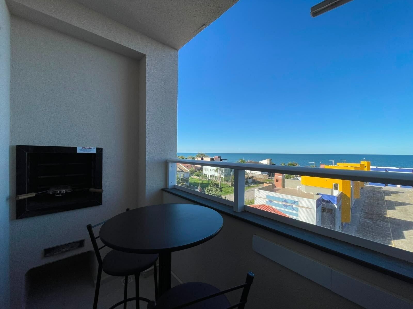 A balcony with a table and chairs, a mounted television, and a view of the sea and buildings.