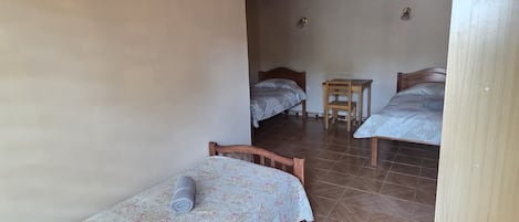Una habitación con dos camas de madera, una mesita y un cesto de basura.