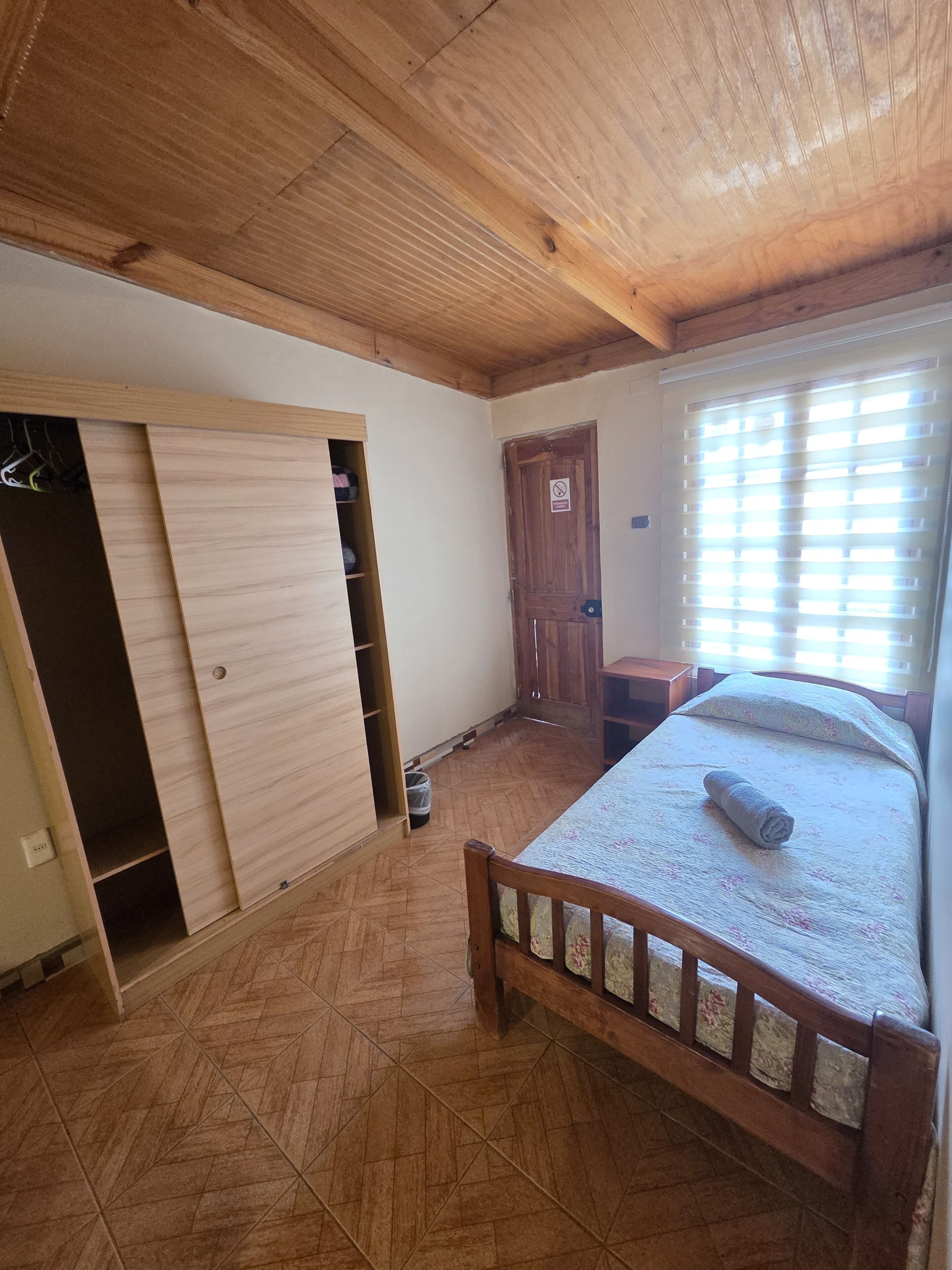 A bedroom with a wooden bed, a wardrobe, and a window with blinds.