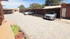 Un patio empedrado con dos coches aparcados, un edificio de ladrillo y una zona cubierta.