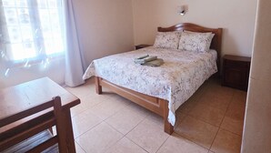 Un dormitorio con techo de madera, una cama con colcha estampada, una mesita de noche y un escritorio de madera con una silla.