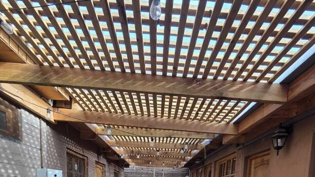 Un patio al aire libre con bancos de madera, suelo de baldosas y una pérgola de madera.