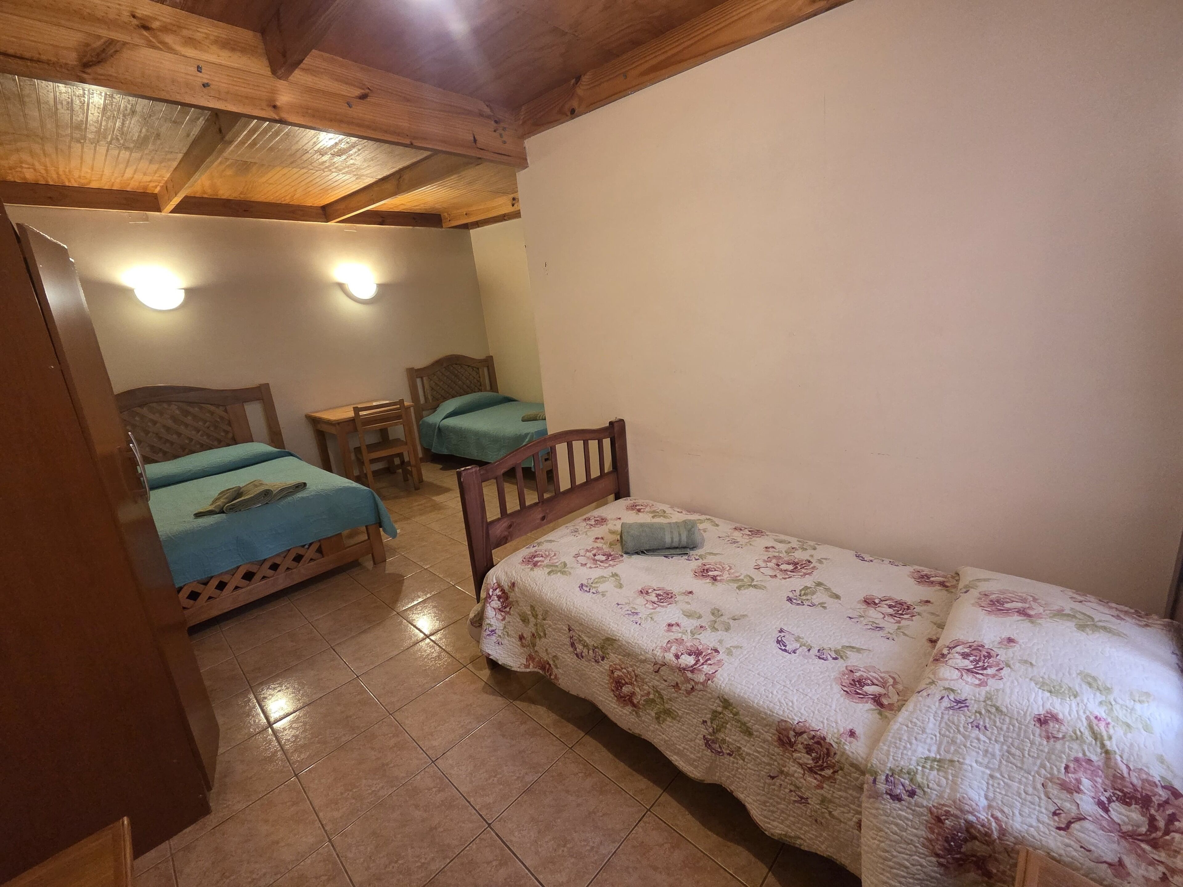 A room with two beds, a wooden ceiling, and a tiled floor.