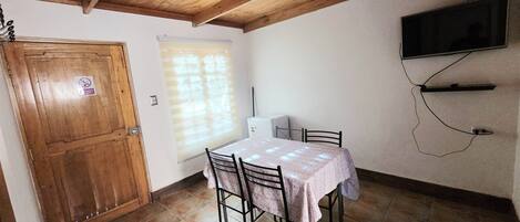 A dining area with a table, chairs, a ceiling fan, a TV mounted on the wall, and a door with a sign.