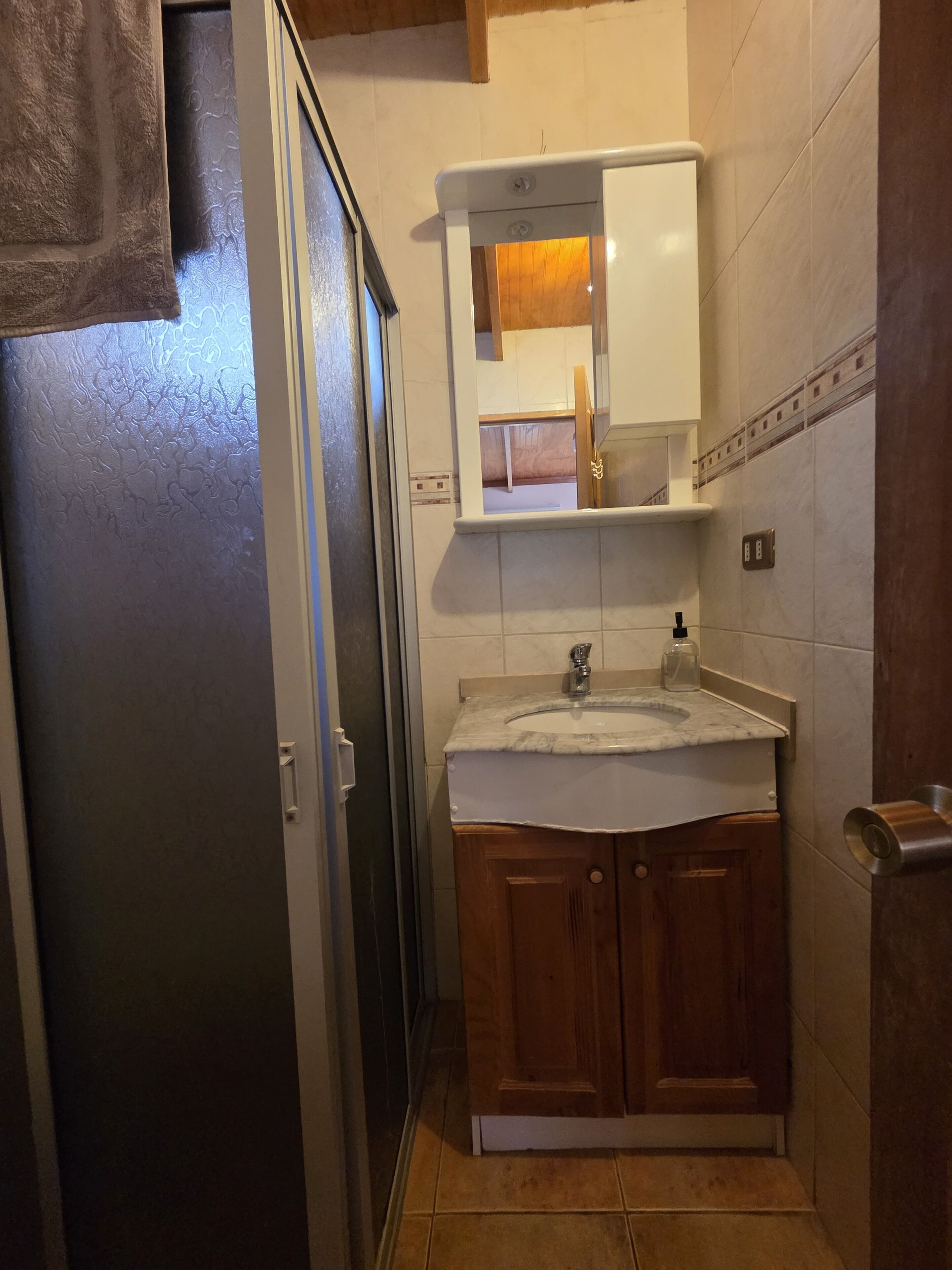 A bathroom with a sink, mirror, cabinet, and towel hanging on the door.