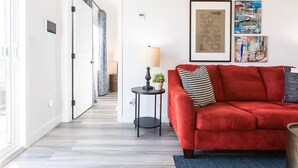 Een moderne woonkamer met een rode bank, een klein bijzettafeltje met een lamp, en twee ingelijste kunstwerken aan de muur.