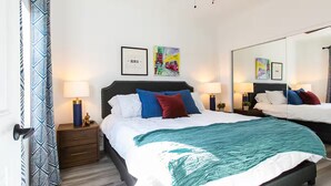 Een hotelkamer met een groot bed, twee nachtkastjes, een spiegel en kunstwerken aan de muur.
