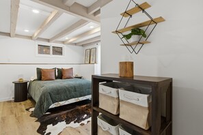 A bedroom with a bed, a wooden shelf with storage bins, a cowhide rug, and a wall-mounted plant. - Hot Tub + Lake Views + Fire Pit - Private Retreat (Osage Beach)