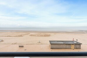 Blick auf einen Strand mit einem Gebäude, einer Bank und einem Verbotsschild für Schwimmen.