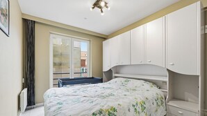 Une chambre à coucher avec un lit, une fenêtre, un radiateur et des armoires blanches.