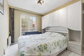Ein Schlafzimmer mit Bett, Fenster, Heizkörper und weißen Schränken.