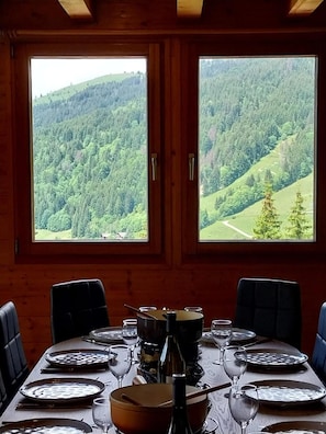 A wooden interior with a dining table set for four, large windows with a forest view, and a rustic ambiance. - Chalet, wifi, balcony, fireplace or stove, parking, tv, 124m², Les Gets (Les Gets)