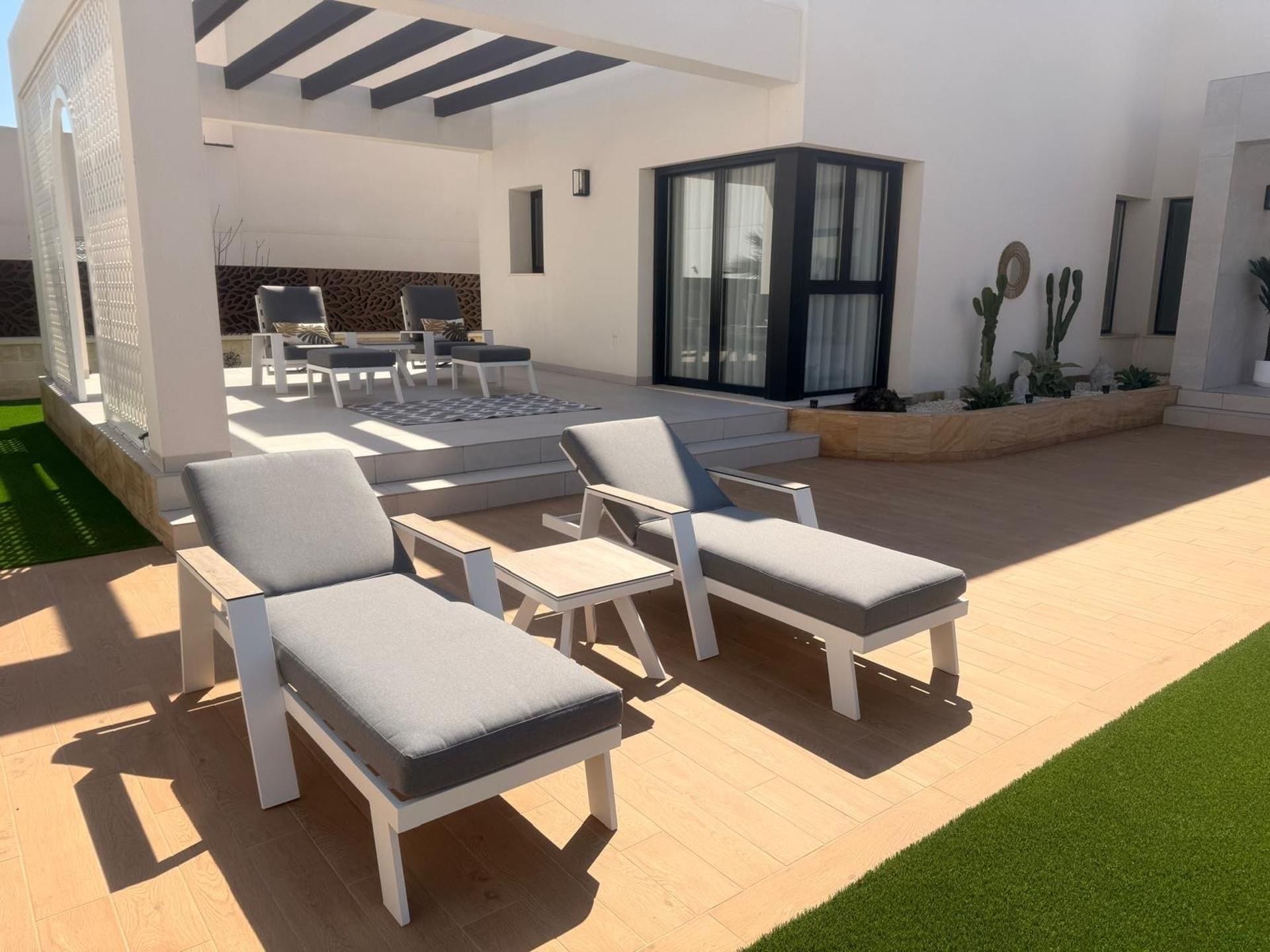 A modern outdoor seating area with lounge chairs and a table, surrounded by a well-maintained lawn and a building with large windows.