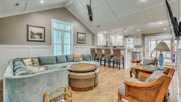 A spacious living area with a sectional sofa, wicker chairs, a dining table, and a kitchen in the background. - Walk to Beach & Parks! Coastal Haven in Oak Island (Oak Island)