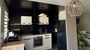Eine kleine Küche mit Herd, Backofen und Kühlschrank, einer Pendelleuchte und einem kleinen Topf mit Pflanze.