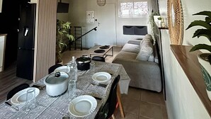 Eine moderne Küche mit Esstisch für vier Personen, einer Treppe zu einem Erkerraum und einem Wohnbereich mit Sofa und großem Spiegel.