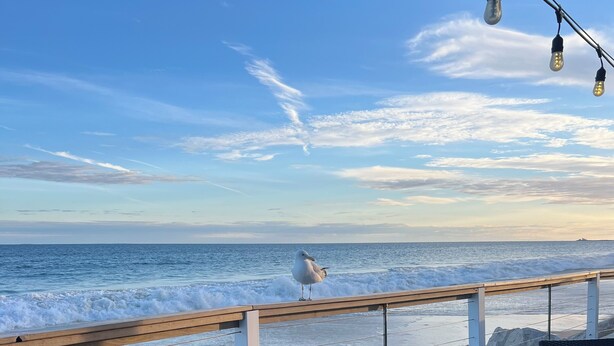 Une terrasse en bord de mer avec une balustrade en bois, un espace salon et une vue sur l’océan.