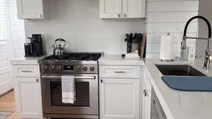 Une cuisine moderne avec des meubles blancs, des appareils en acier inoxydable, une cuisinière à gaz, une machine à café et un évier avec un tuyau noir.