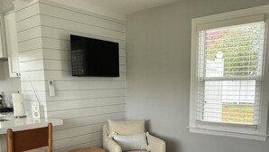 Une cuisine moderne avec des meubles blancs, une table à manger en bois, un tabouret en bois et un fauteuil beige.