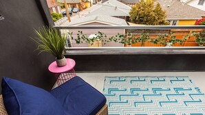 A balcony with a blue cushioned seating area, a woven rug, and a potted plant. - Spacious Studio – Balcony, Desk, A/C & Kitchen (San Diego)