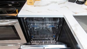 An open dishwasher in a kitchen with a white marble countertop and stainless steel appliances. - Spacious Studio – Balcony, Desk, A/C & Kitchen (San Diego)