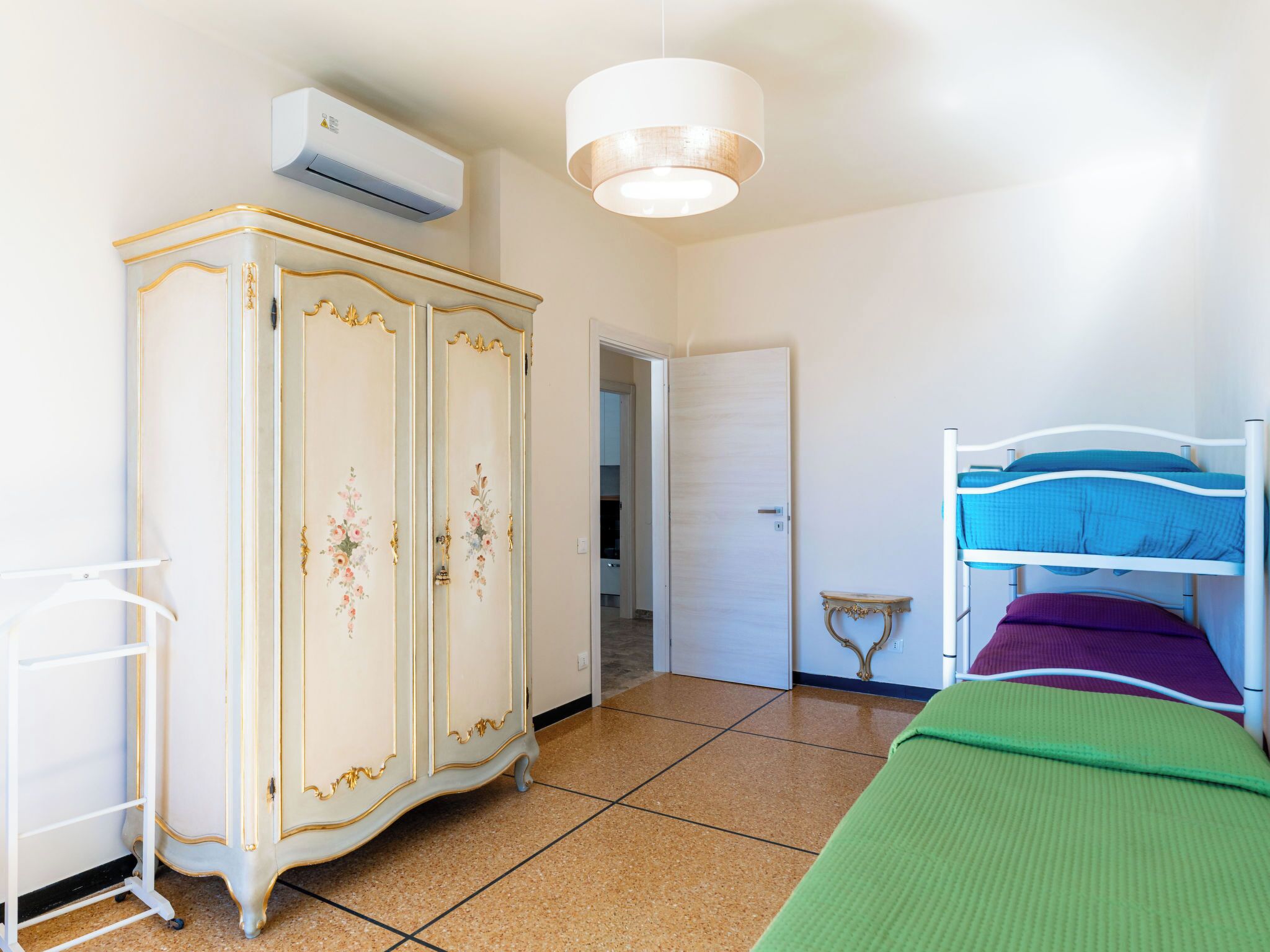 Une chambre avec un lit superposé, une armoire ornée de motifs floraux, une petite table et un appareil de climatisation.