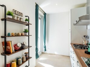 A modern kitchen with a gas stove, a built-in oven, and a stainless steel range hood. There is a wooden shelf unit with various kitchen items and a potted plant. - Orizzonte Blu Alassio by Interhome (Alassio)
