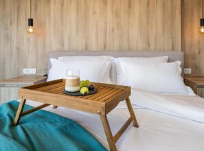 A hotel room with a wooden headboard, a bedside table with a lamp, a bed with white linens, and a tray with a glass of milk and grapes on a wooden table.