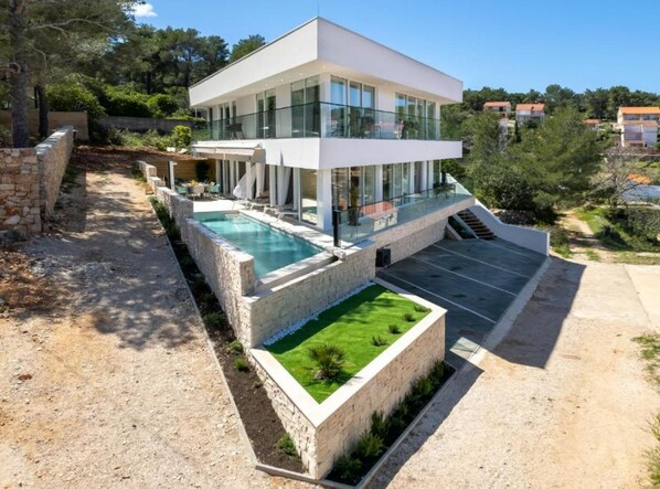 A modern two-story house with a swimming pool, a covered patio, and a landscaped garden.