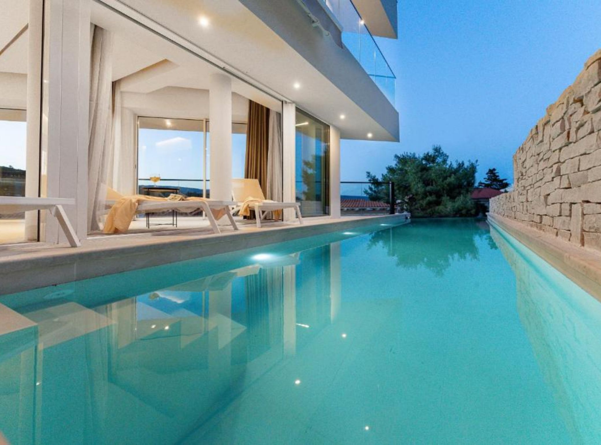 A modern poolside area with lounge chairs and a clear view of the sea.