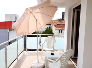 A balcony with a white umbrella, white chairs, and a small table. - Comfort Apartments N (Sutomore)