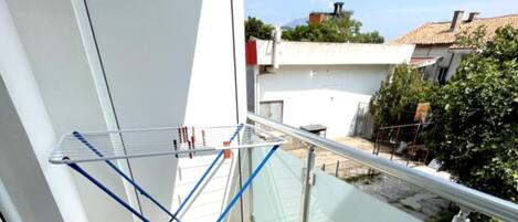 Un balcon doté d’un étendoir, d’une rambarde en métal et offrant une vue sur un quartier résidentiel avec des maisons et des arbres.