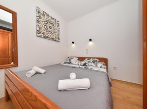 A bedroom with a wooden bed, grey bedding, a decorative wall piece, and two wall-mounted lights. - Privlaka Sunset Apartments (Privlaka)