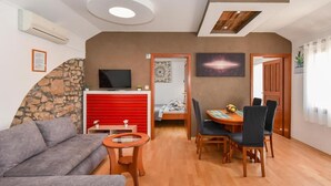 A modern living room with a sofa, a small table, a TV, and a dining area with chairs and a table. - Privlaka Sunset Apartments (Privlaka)