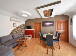 A living room with a sofa, a dining table with chairs, a TV, and a fireplace. - Privlaka Sunset Apartments (Privlaka)
