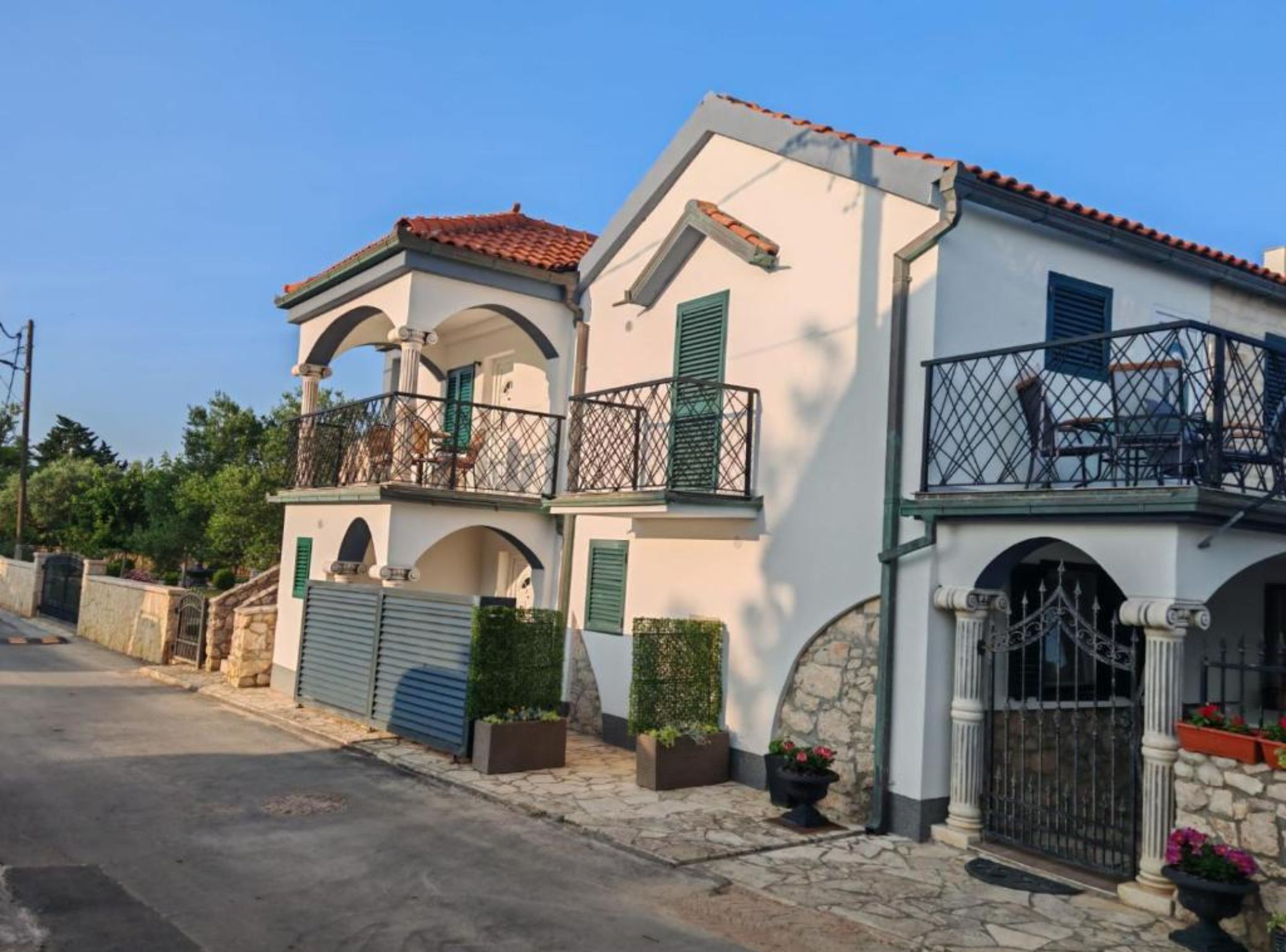 A two-story house with a balcony, stone walls, and a metal gate.