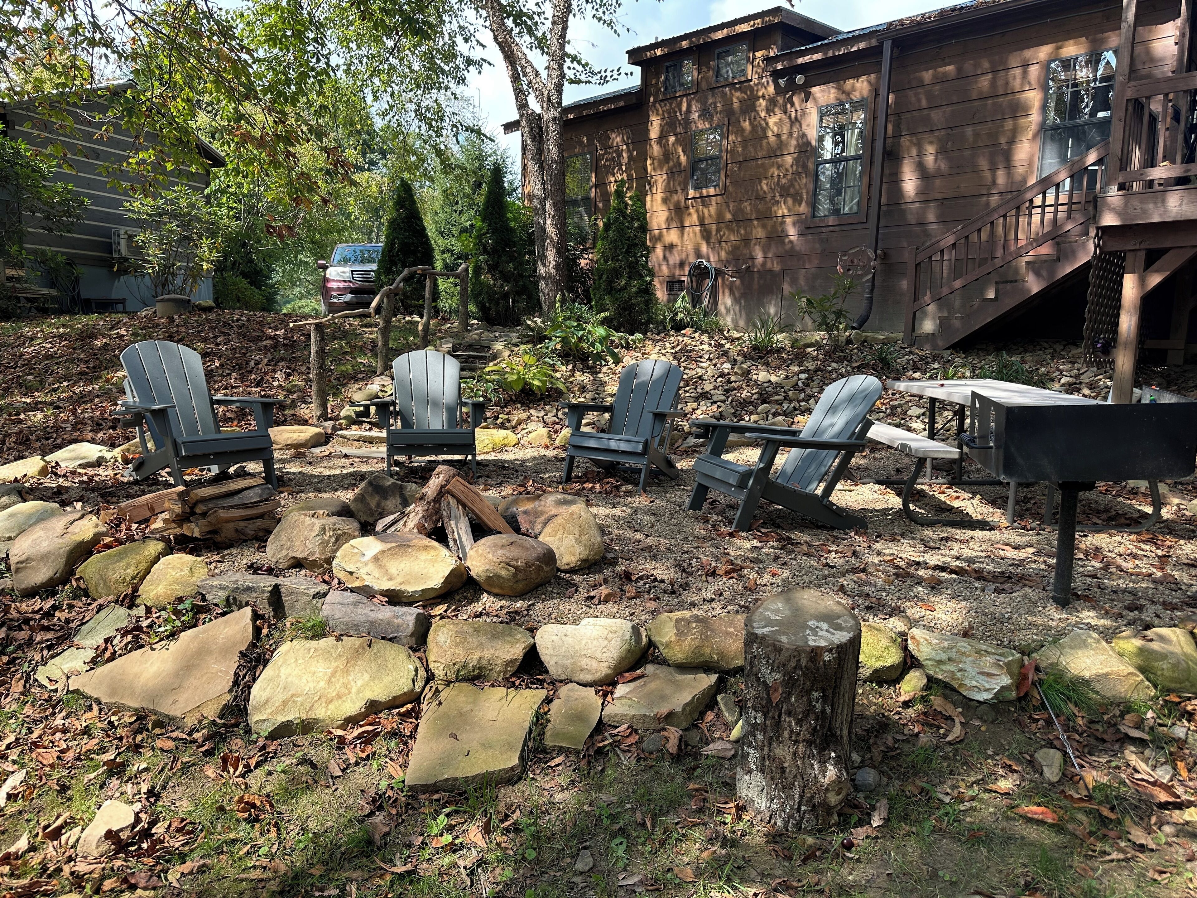 Eine Terrasse mit Adirondack-Stühlen, einem Feuerkorb und einer Steinmauer.