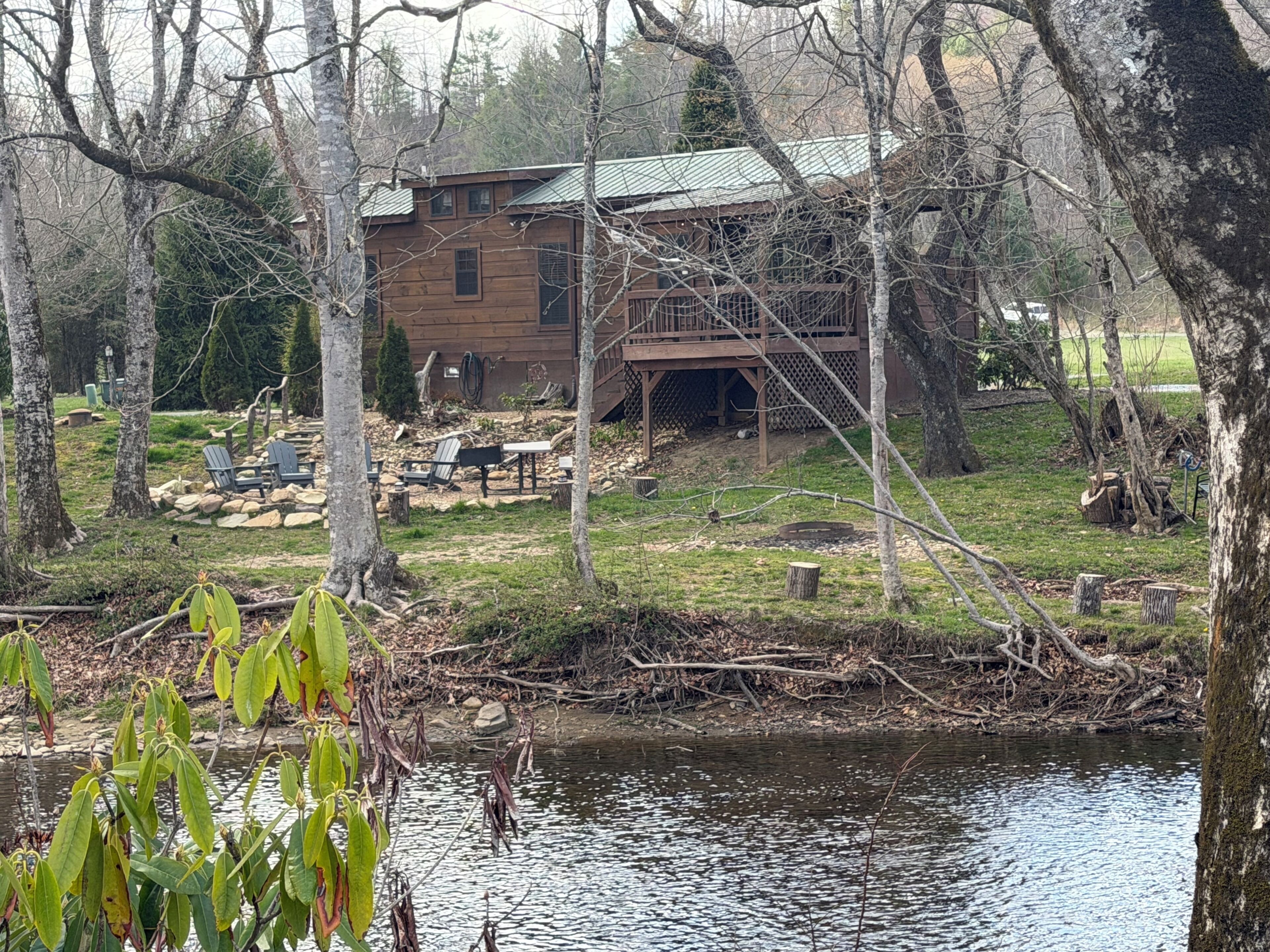 A cabin with a deck, surrounded by trees and a body of water.