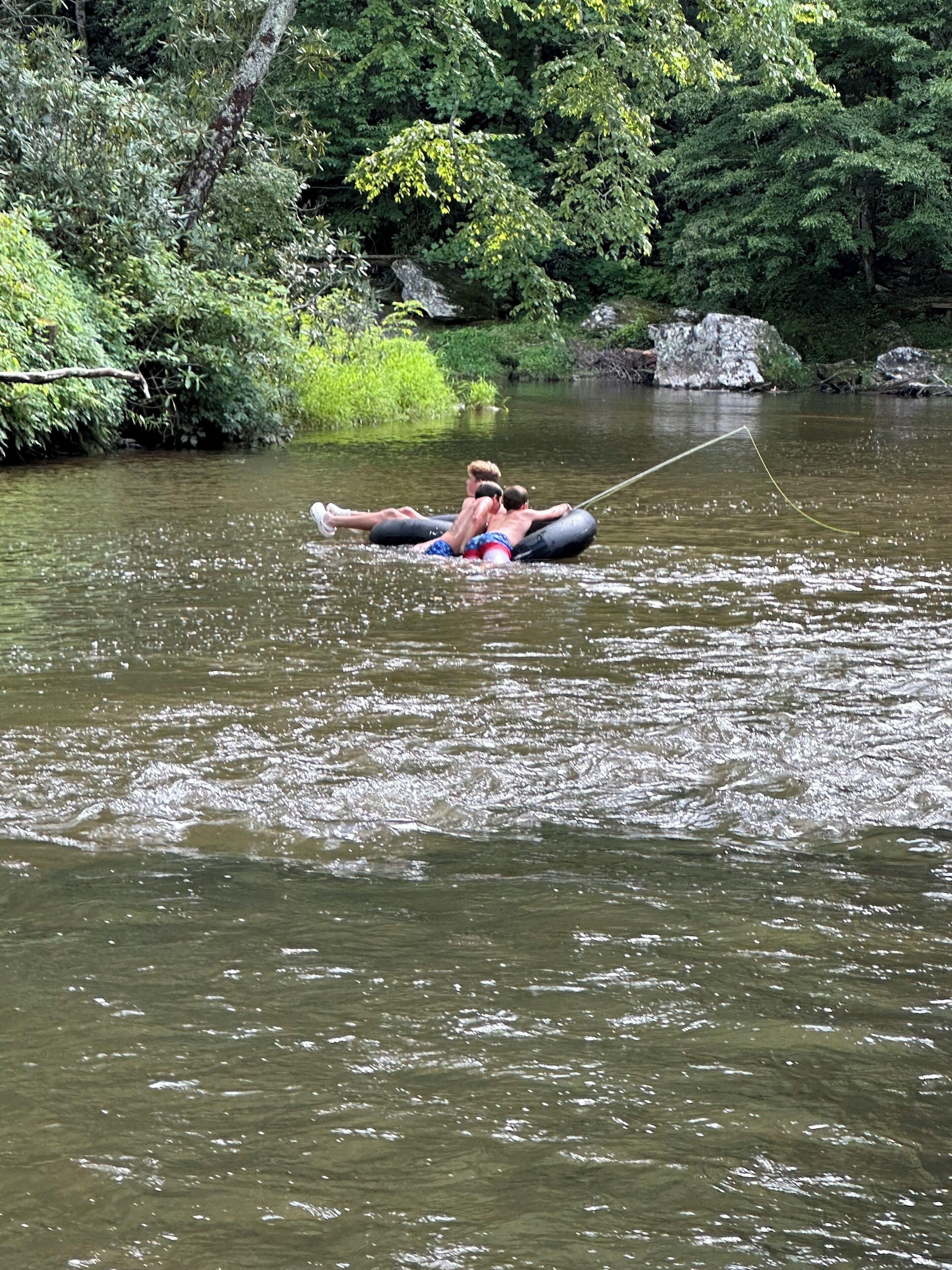 Two people floating on a raft in a river surrounded by dense greenery.