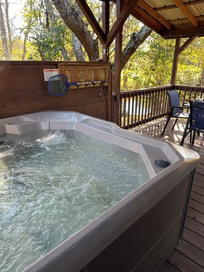 A hot tub on a wooden deck with a wooden railing and a chair.