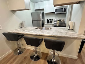 A kitchen with a marble countertop, stainless steel appliances, and three black bar stools.
